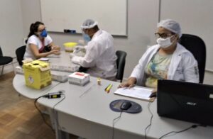 Foto da testagem referente à Covid-19. Os técnicos Gerson Pereira (à esquerda, no manejo dos equipamentos) e Socorro Guedes (no registro) estão atendendo os discentes, docentes, técnicos e terceirizados da UFC.